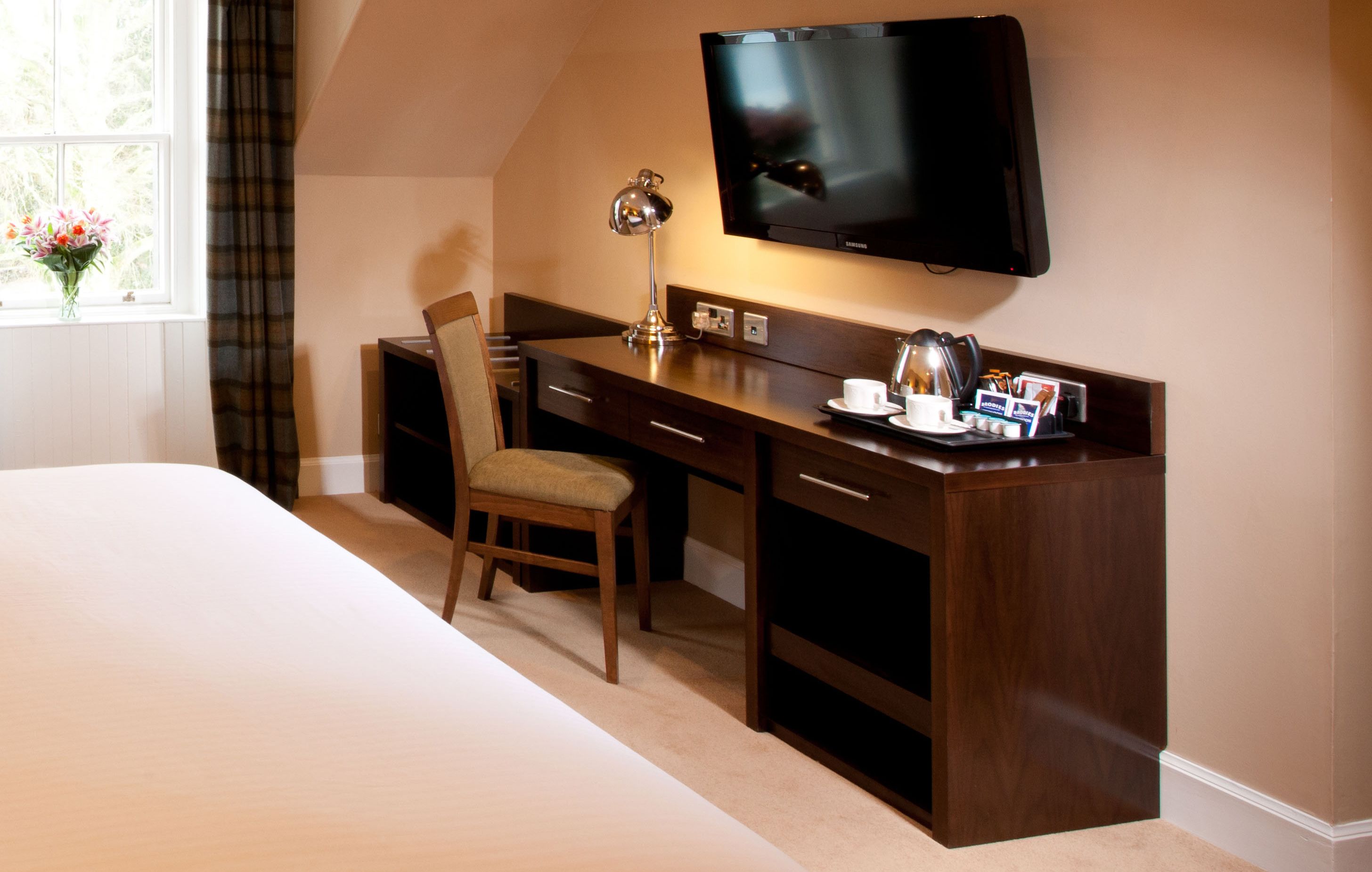 A hotel room with a bed, a desk with a chair, a television, and a window with curtains.