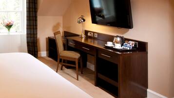 A hotel room with a bed, a desk with a chair, a television, and a window with curtains.
