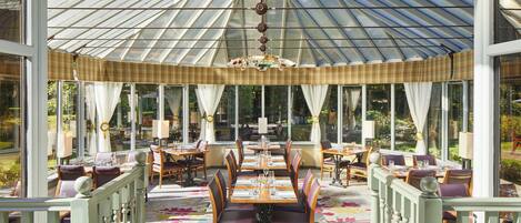 A conservatory with a glass ceiling, furnished with tables and chairs, and a patterned carpet.