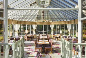 A conservatory with a glass ceiling, furnished with tables and chairs, and a patterned carpet.