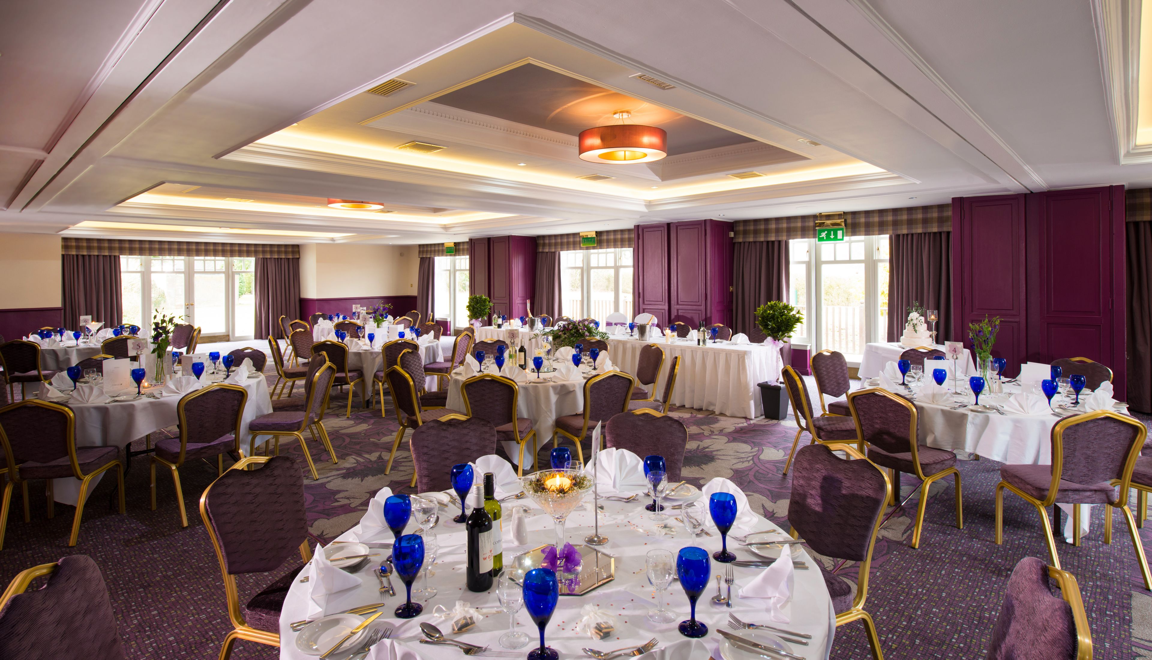 Un salón de banquetes con mesas redondas, manteles blancos y sillas moradas.