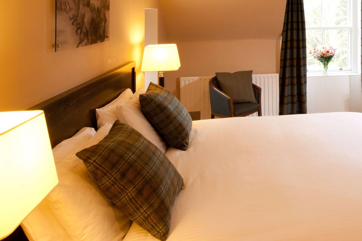 A hotel room with a large bed, two bedside lamps, a chair, and a window with curtains.