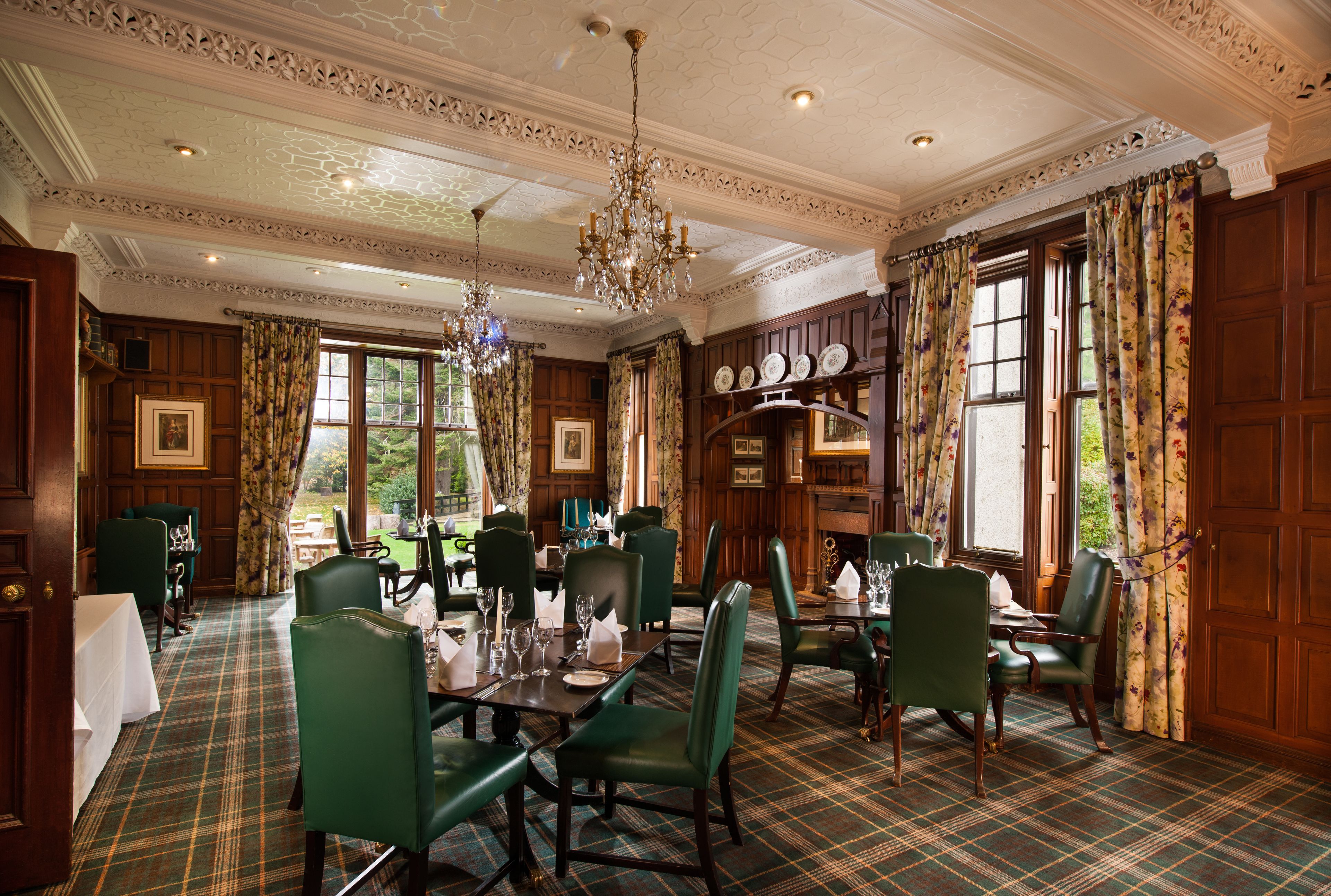 A formal dining room with green upholstered chairs, a chandelier, and a plaid carpet.