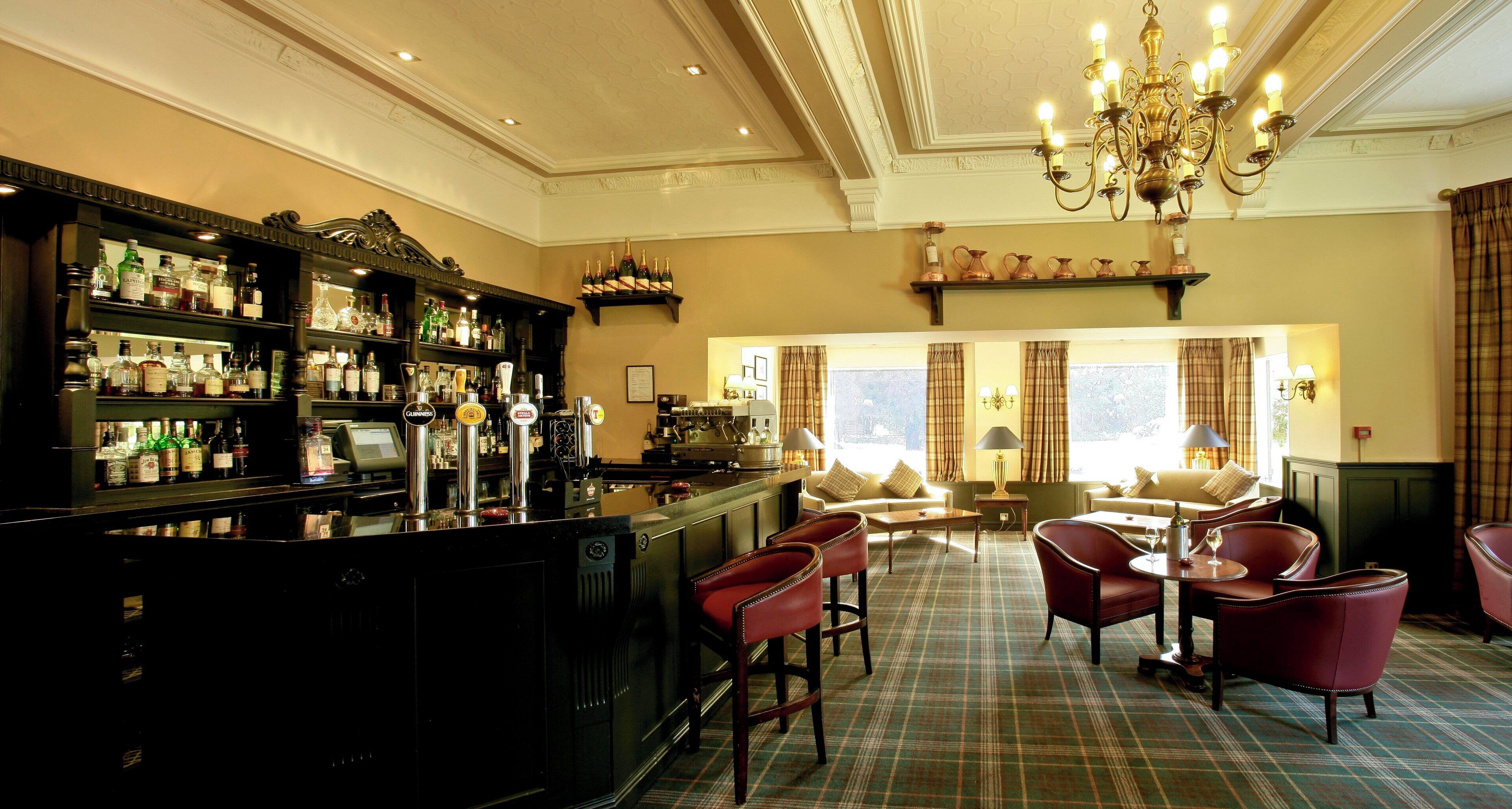 A bar area with a variety of liquor bottles and a cash register. There are red leather chairs and a sofa in the seating area.
