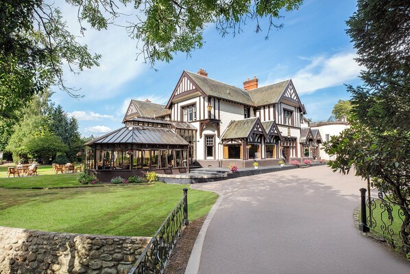 A large, traditional building with a symmetrical facade, a covered patio area, and a well-maintained lawn.