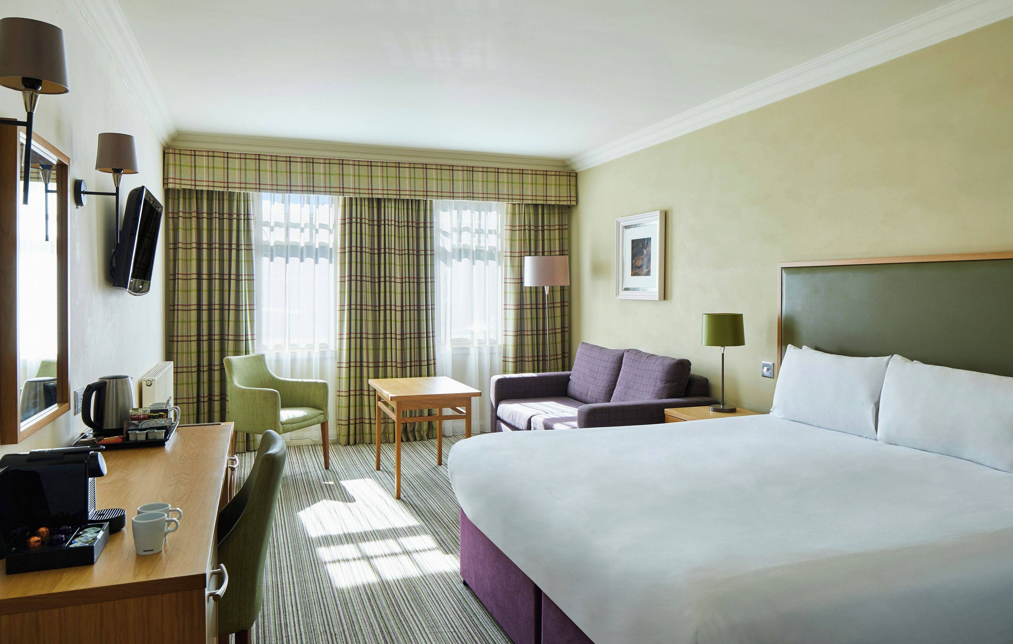 Ein Hotelzimmer mit Bett, Schreibtisch mit Telefon, Stuhl, Tisch und einem Fenster mit Vorhängen.