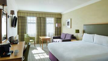 Ein Hotelzimmer mit Bett, Schreibtisch mit Telefon, Stuhl, Tisch und einem Fenster mit Vorhängen.