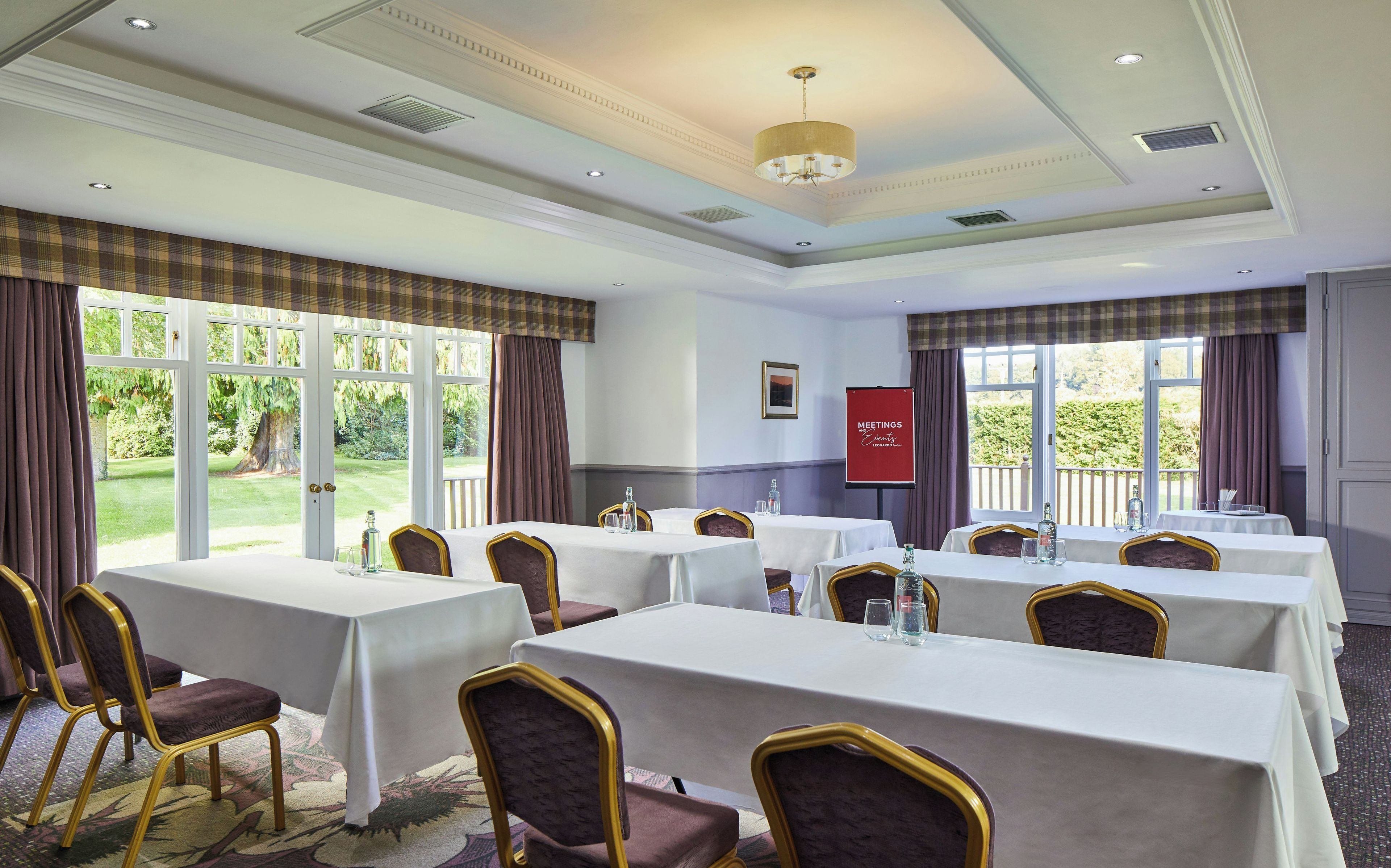 A conference room with multiple tables and chairs, large windows with curtains, and a red banner on the wall.