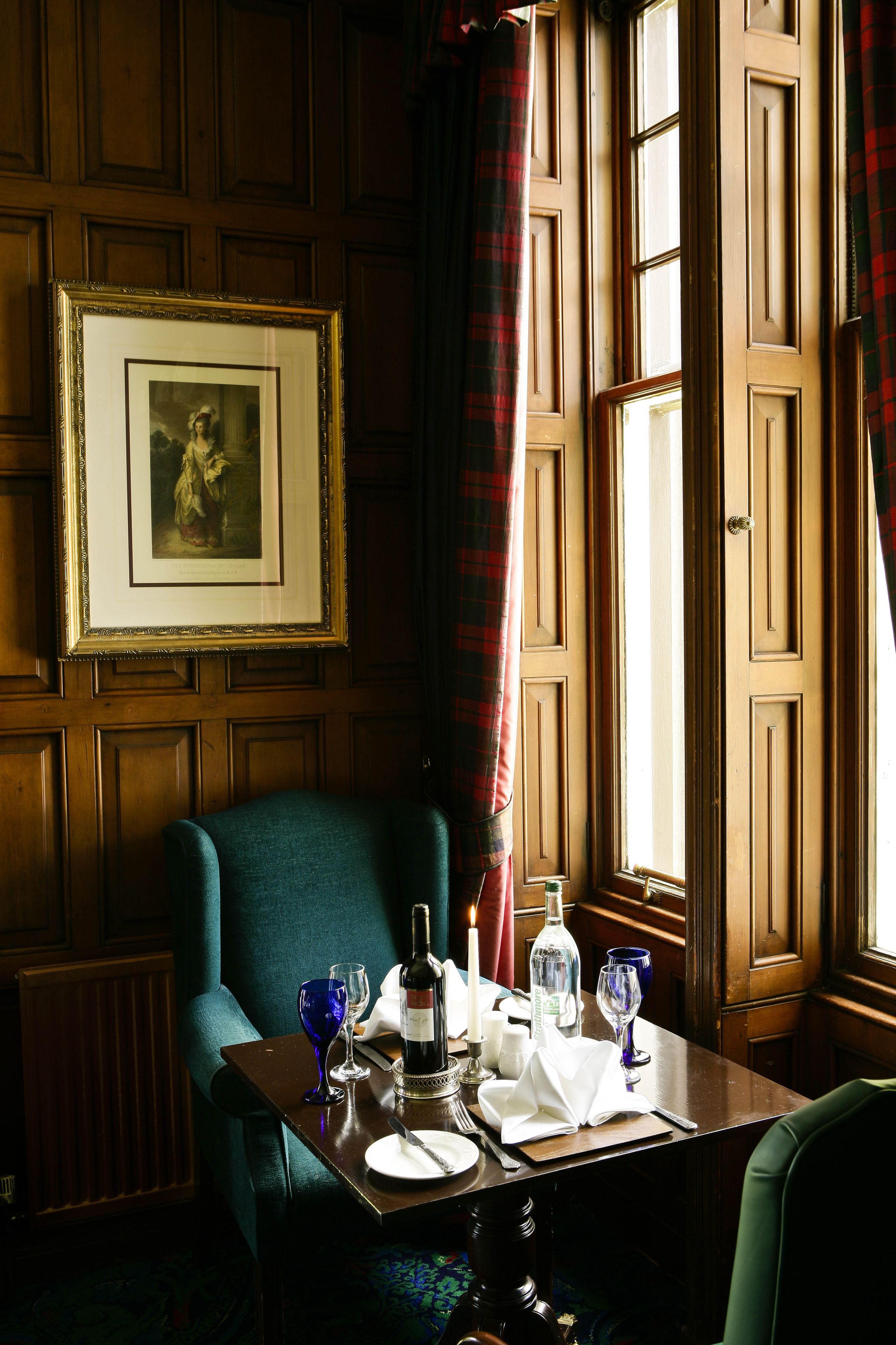 A dining table set with a bottle, glasses, and a framed picture on the wall.