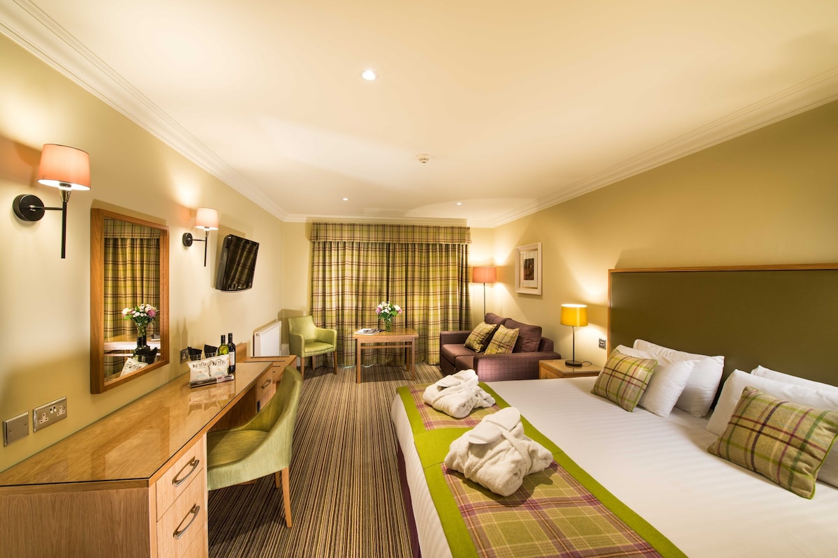 A hotel room with a bed, a desk, a chair, a sofa, and a small table.