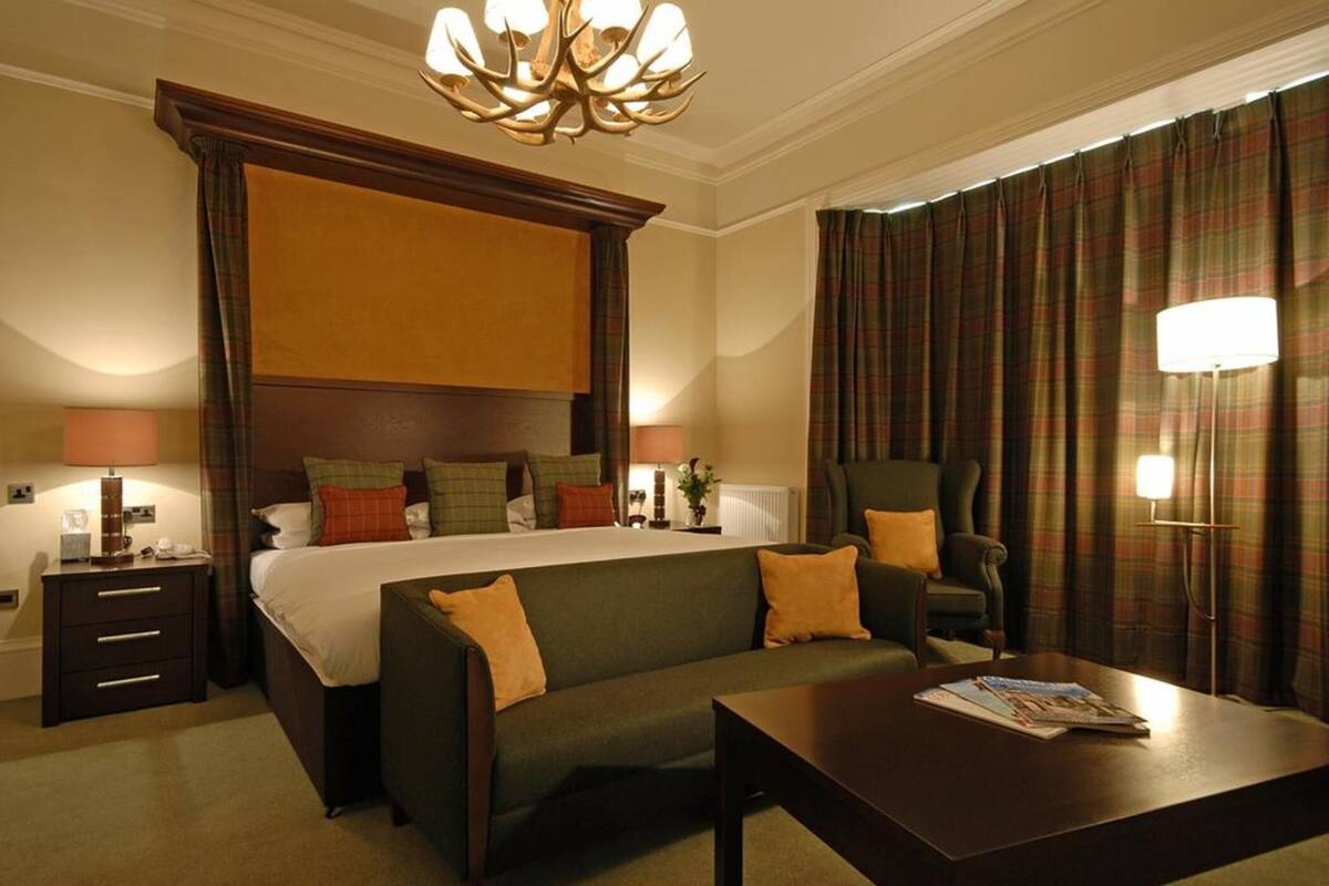 A hotel room with a large bed, a sofa, a coffee table, a chair, a lamp, and curtains.