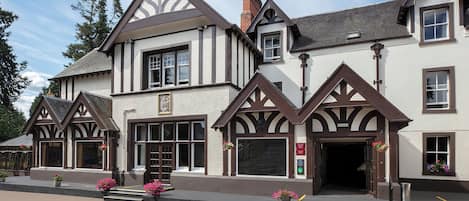 A traditional Tudor-style building with a symmetrical facade, large windows, and a central entrance.