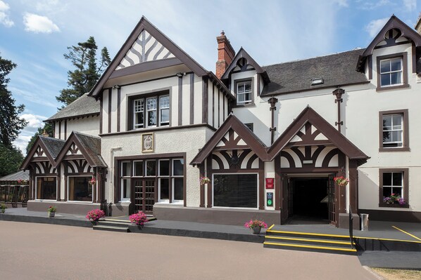 A traditional Tudor-style building with a symmetrical facade, large windows, and a central entrance.