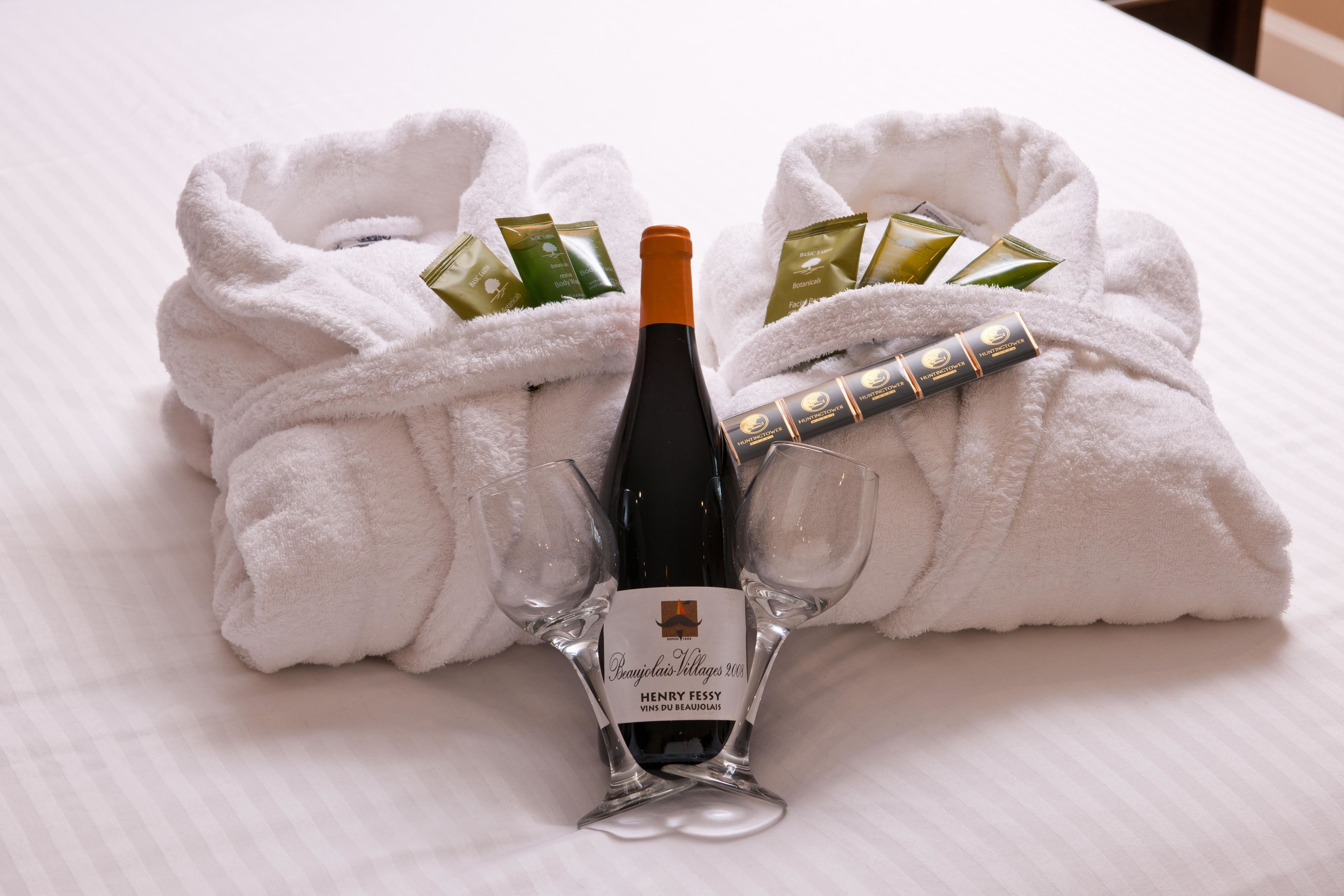 A bottle of Henry Feessy wine, two glasses, and toiletries in a white robe on a bed.