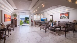 A spacious living area with a television, seating, and a view of the outdoors. - Sun Rise Hotel (Aristotelis)