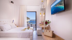 A hotel room with a bed, a small table with drinks, a bench, and a TV displaying a scenic view. - Sun Rise Hotel (Aristotelis)
