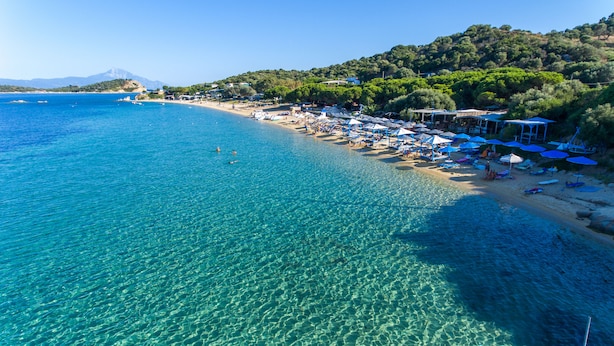 A beach with clear blue water, umbrellas, and beach chairs. - Sun Rise Hotel (Aristotelis)