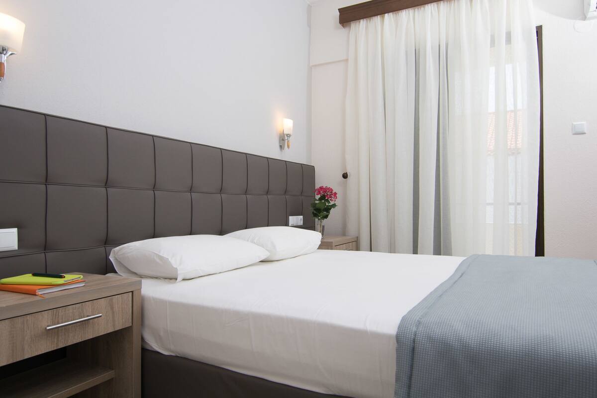 A hotel room with a large bed, a nightstand, a lamp, and a window with curtains.