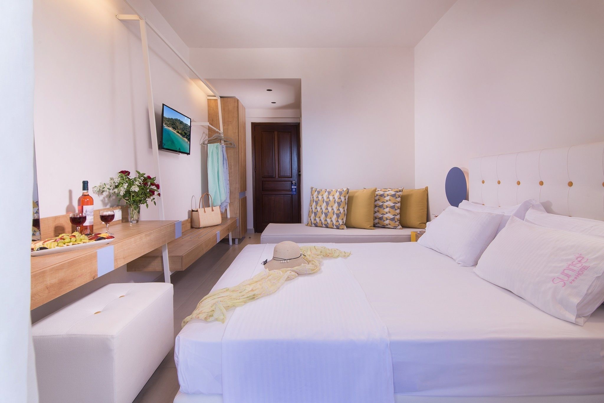 A hotel room with a bed, a bedside table with a bottle and flowers, a TV, and a view of the beach.