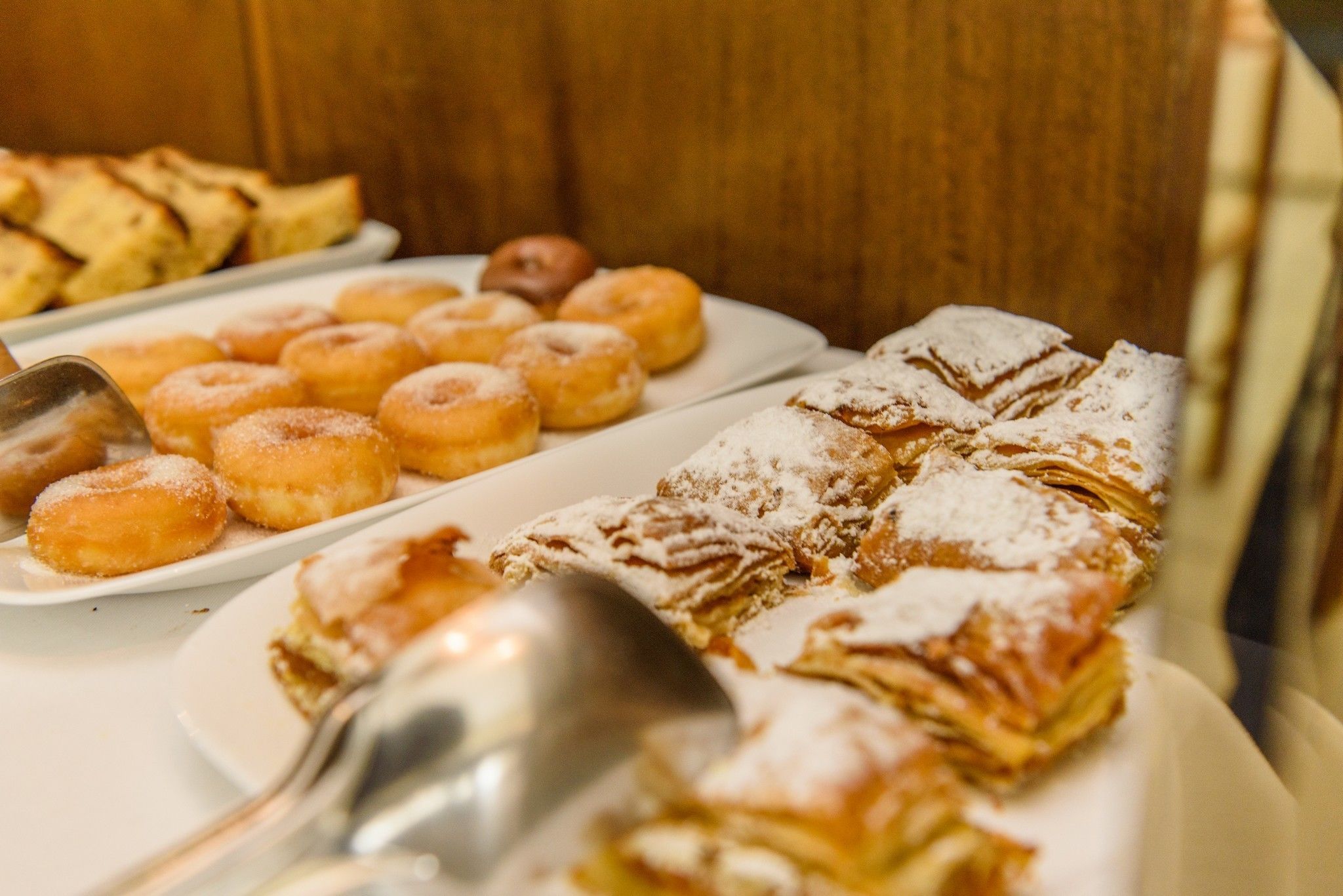 Een buffet met diverse gebakjes, waaronder donuts en een groot gebakje bestrooid met poedersuiker.