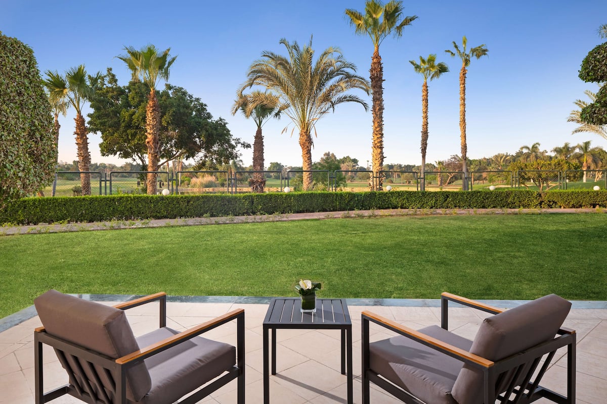 An outdoor seating area with two chairs and a table, surrounded by a well-maintained lawn and tall palm trees.