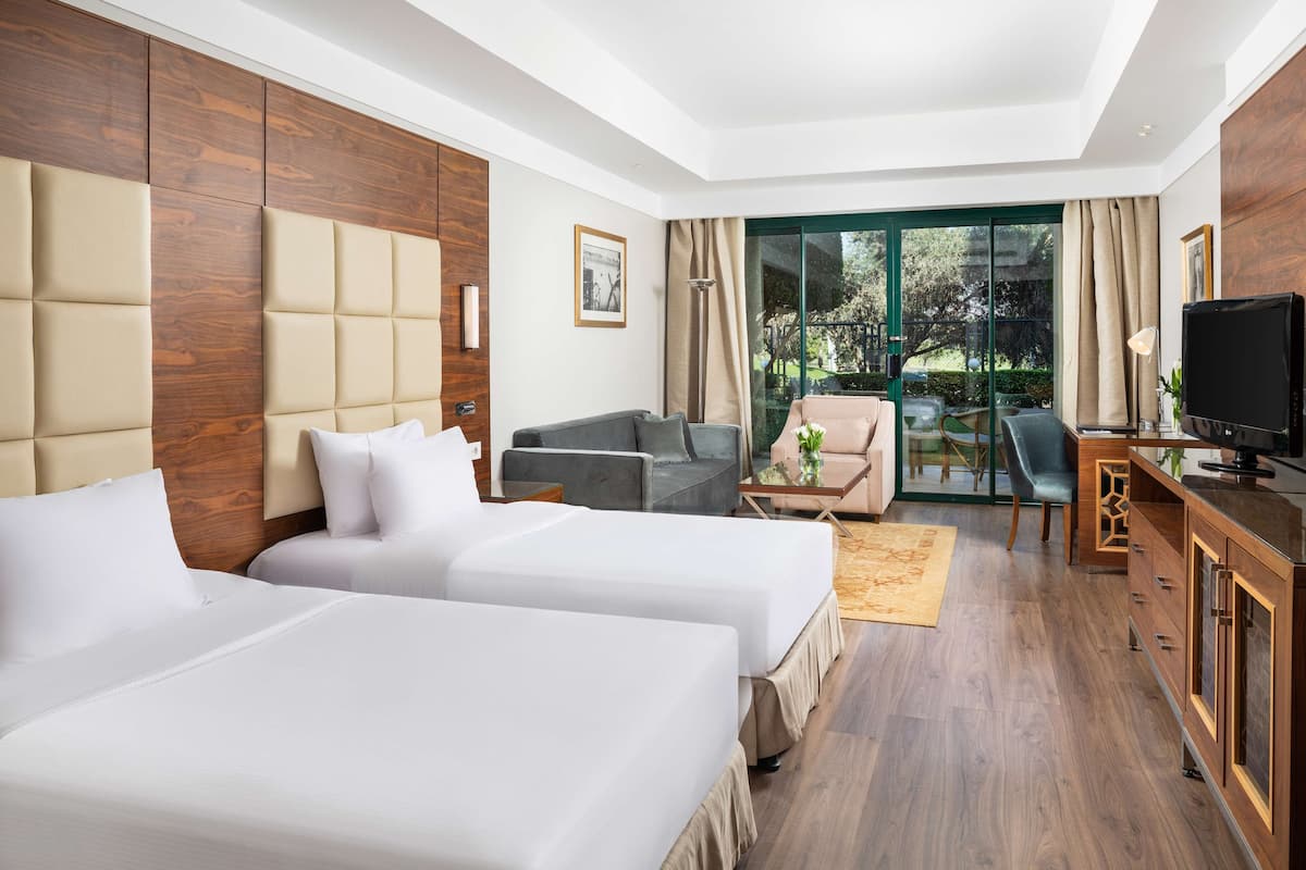 A hotel room with two beds, a sofa, a TV, and a sliding glass door to the outdoors.
