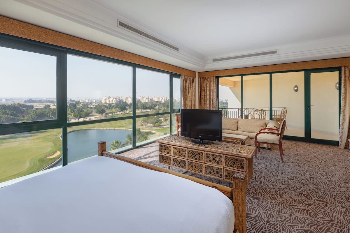 A hotel room with a large bed, a TV, a sofa, and a view of a golf course and cityscape.