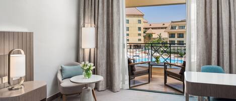 A hotel room with a balcony, a round table, a chair, a sofa, and a lamp.