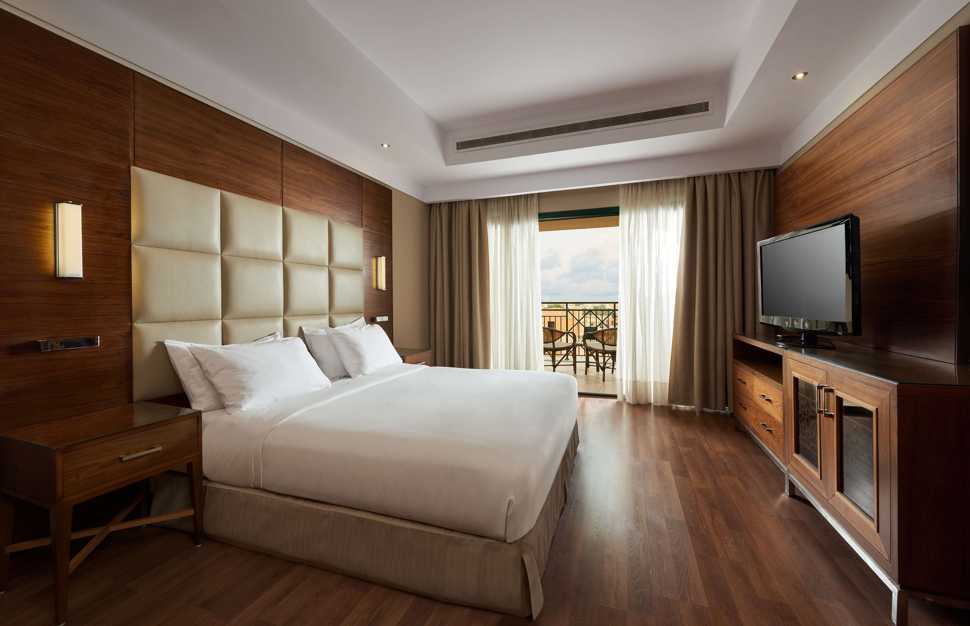 A hotel room with a large bed, wooden paneling, a television, and a balcony with outdoor furniture.