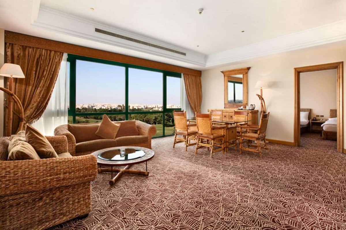 A spacious room with a large window, a dining area with wicker furniture, and a view of the city.