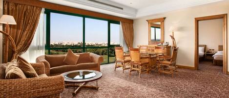 A spacious room with a large window, a dining area with wicker furniture, and a view of the city.
