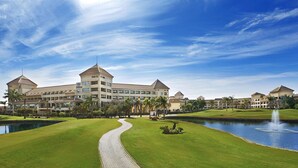 A golf course with a pond, a fountain, and a large hotel building with multiple towers.
