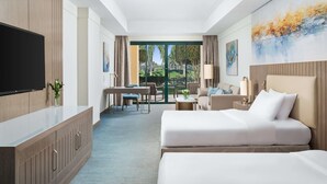 A hotel room with a large bed, a desk with a chair, a sofa, and a TV on a cabinet.