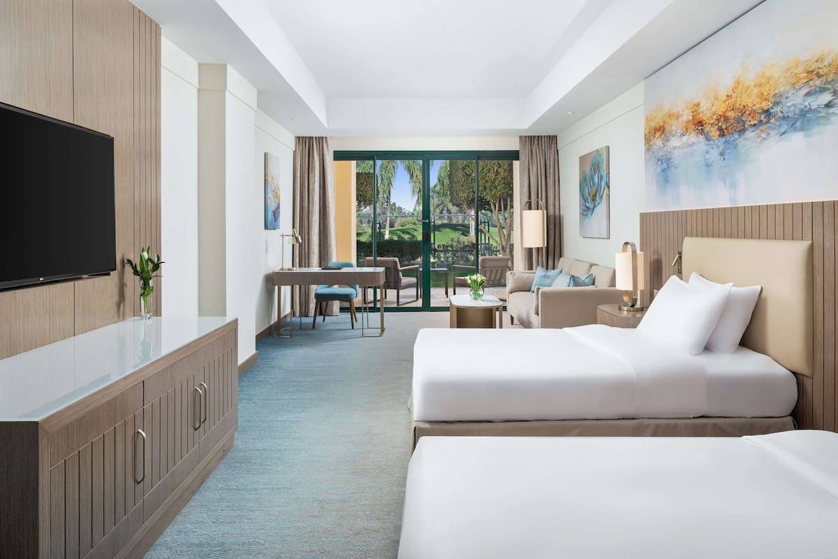 A hotel room with a large bed, a desk with a chair, a sofa, and a TV on a cabinet.