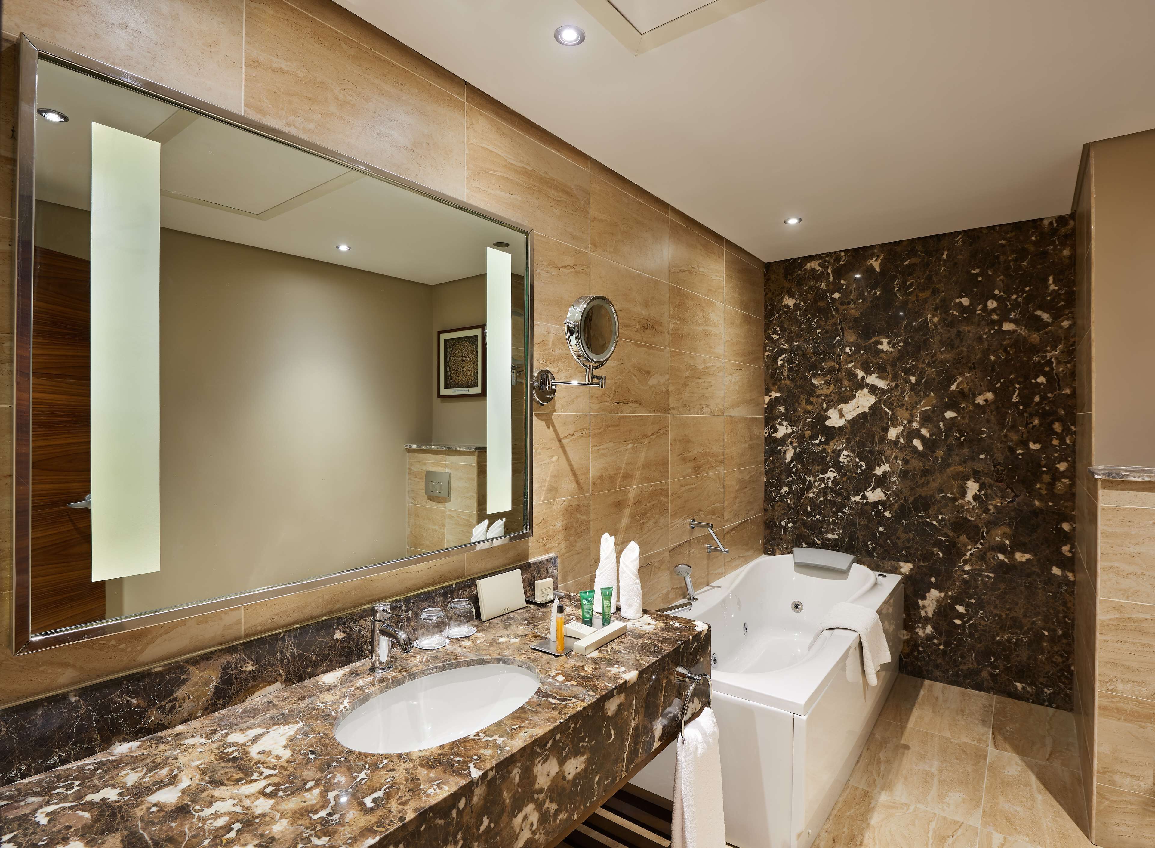 A modern bathroom with a large mirror, a sink, a bathtub, and a vanity with toiletries.