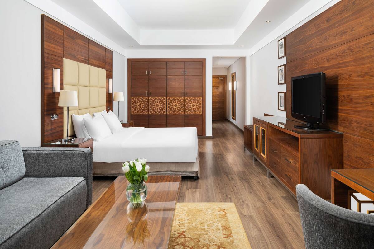 A modern hotel room with a large bed, a sofa, a TV, and a wooden wardrobe.