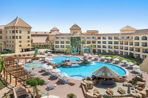 A hotel with a large central pool, multiple balconies, and a well-maintained garden area. - Hilton Pyramids Golf (6th of October City)