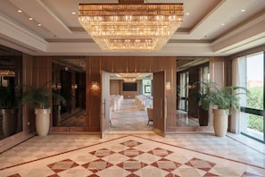 A hotel lobby with a large chandelier, a conference room, and potted plants. - Hilton Pyramids Golf (6th of October City)