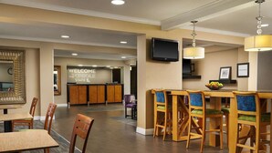 Een hotel lobby met een receptiebalie, een televisie en een bar met stoelen en een schaal fruit.