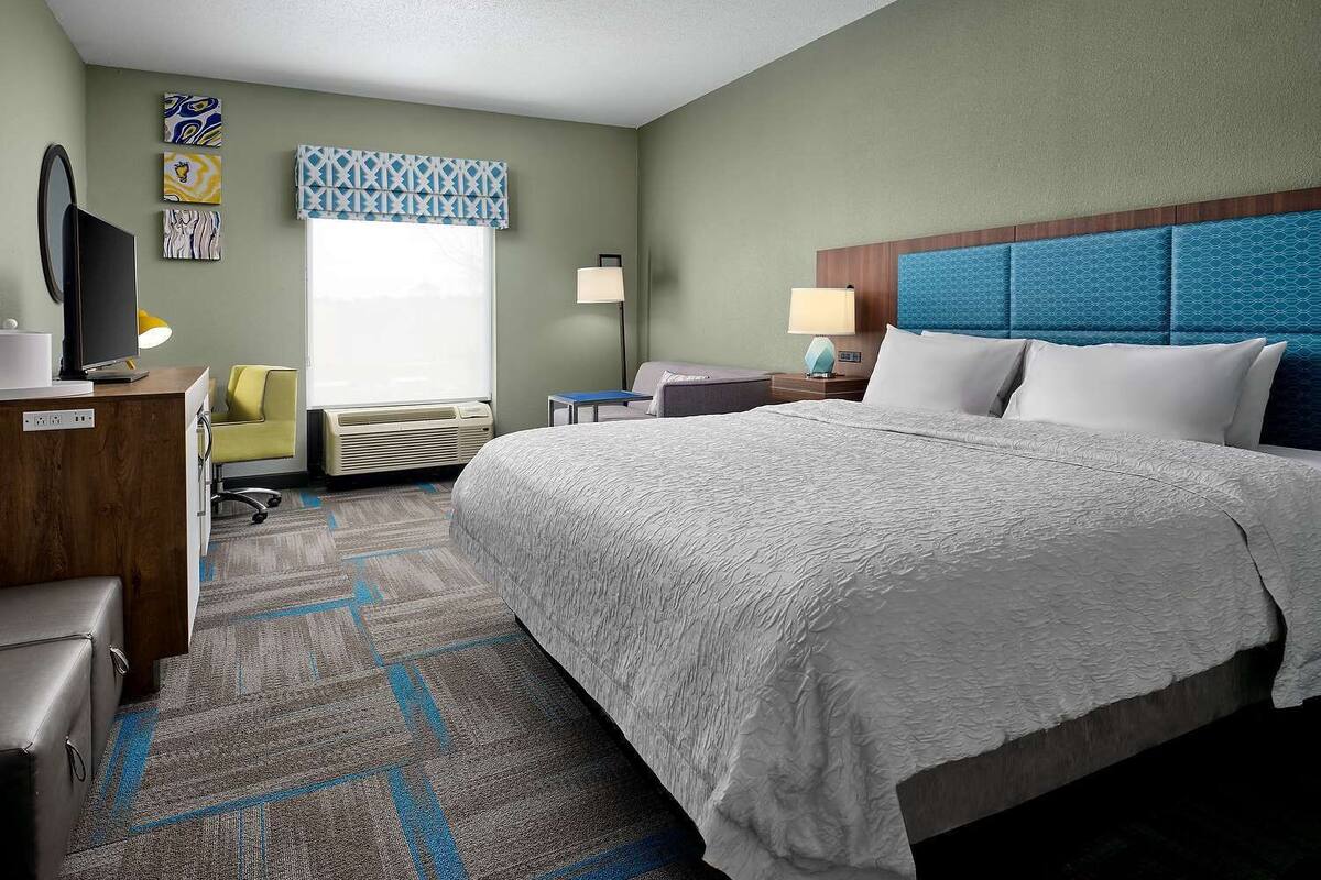 A hotel room with a large bed, a desk with a computer, a chair, a TV, and a window with a view.