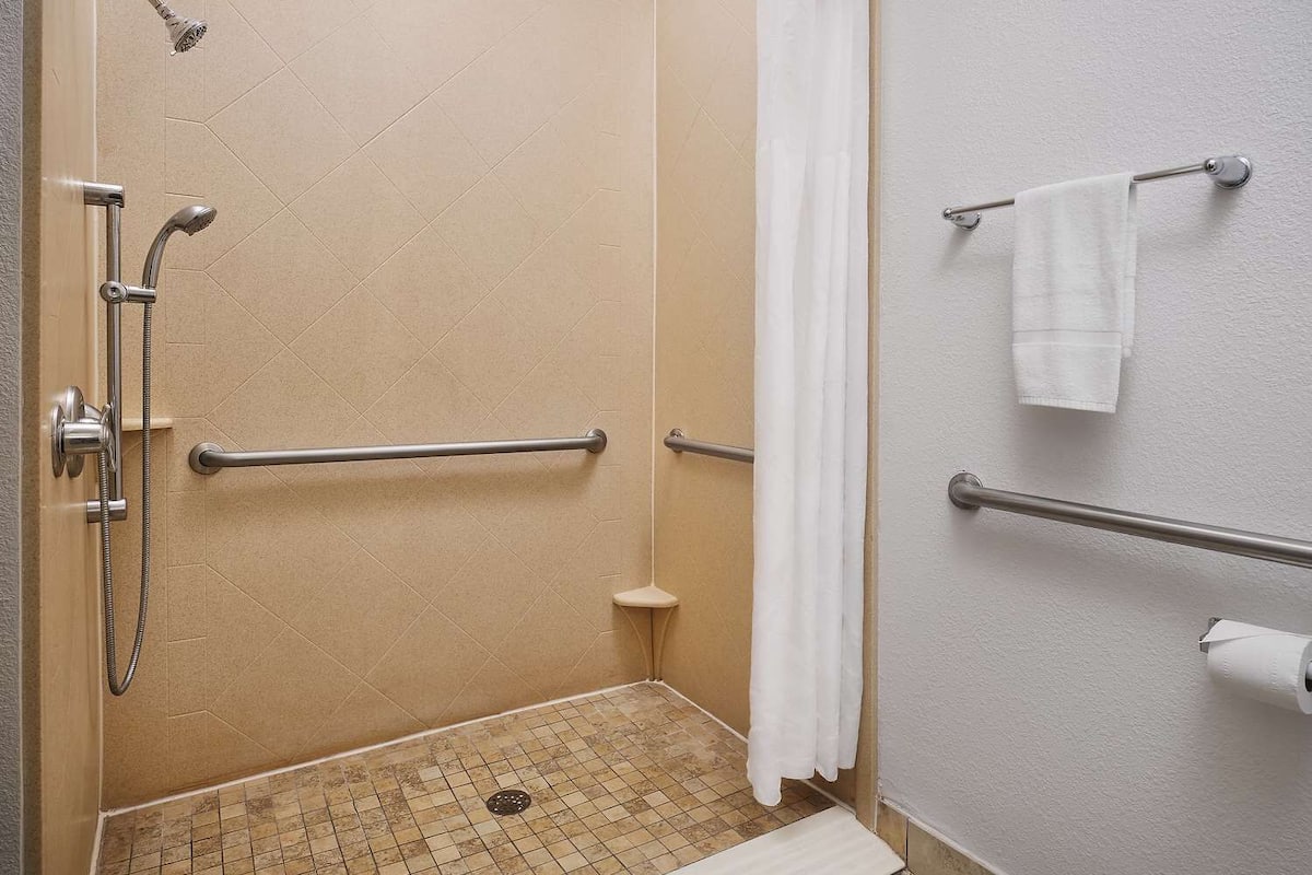 A shower with a handheld showerhead, a handheld showerhead, and a grab bar.