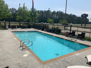A rectangular outdoor swimming pool with a tiled edge, surrounded by a brick deck.