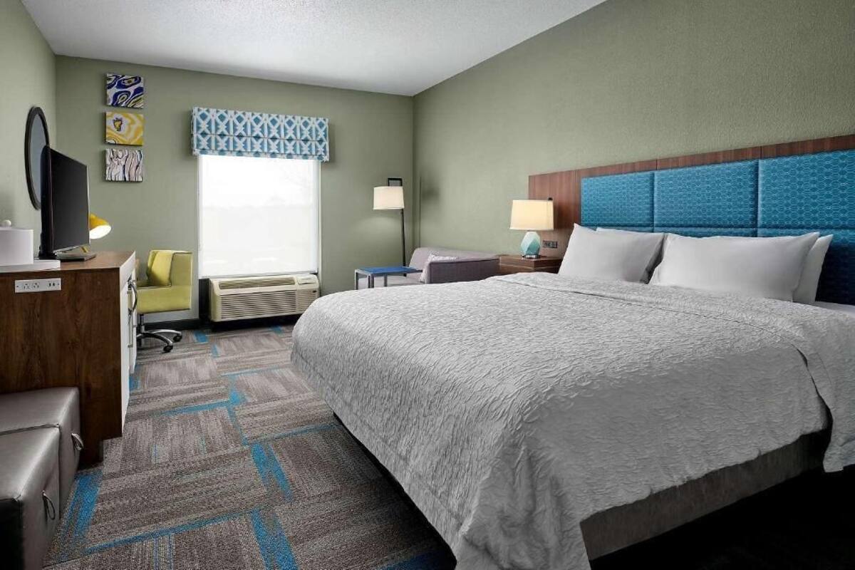 A hotel room with a large bed, a desk with a computer, a chair, and a window with a view.
