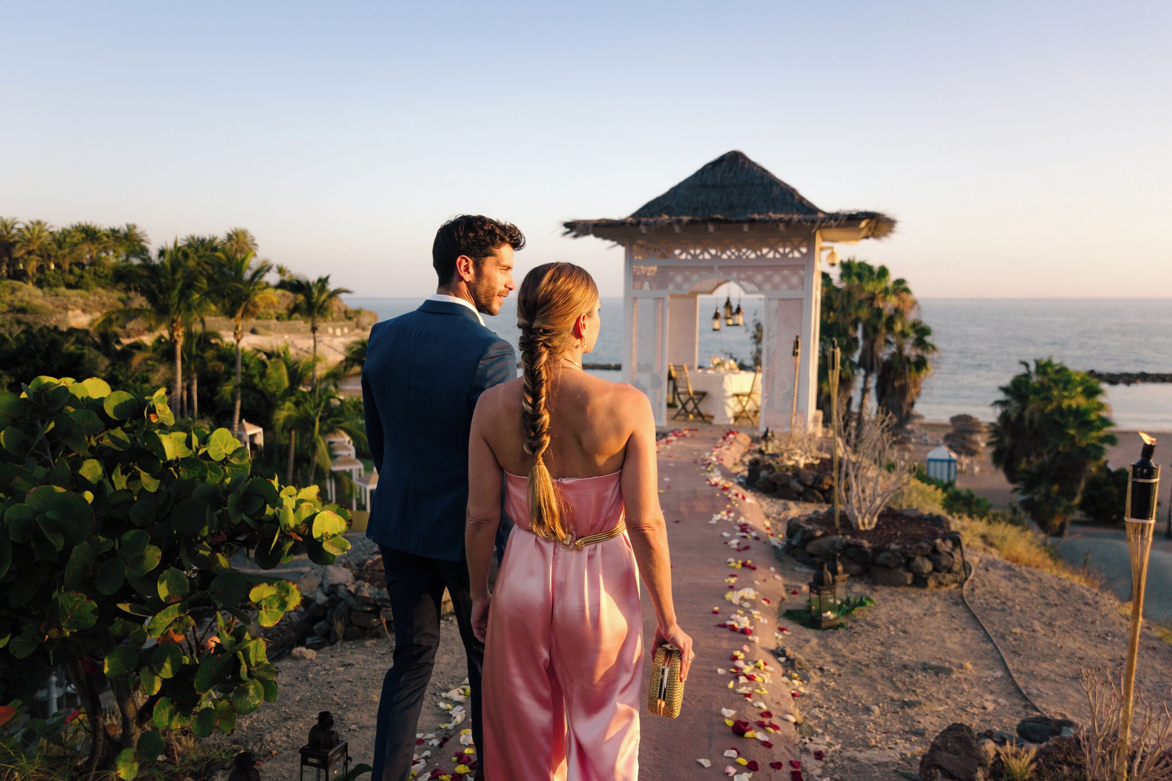 Una pareja caminando por un sendero con un mirador y vista al océano.