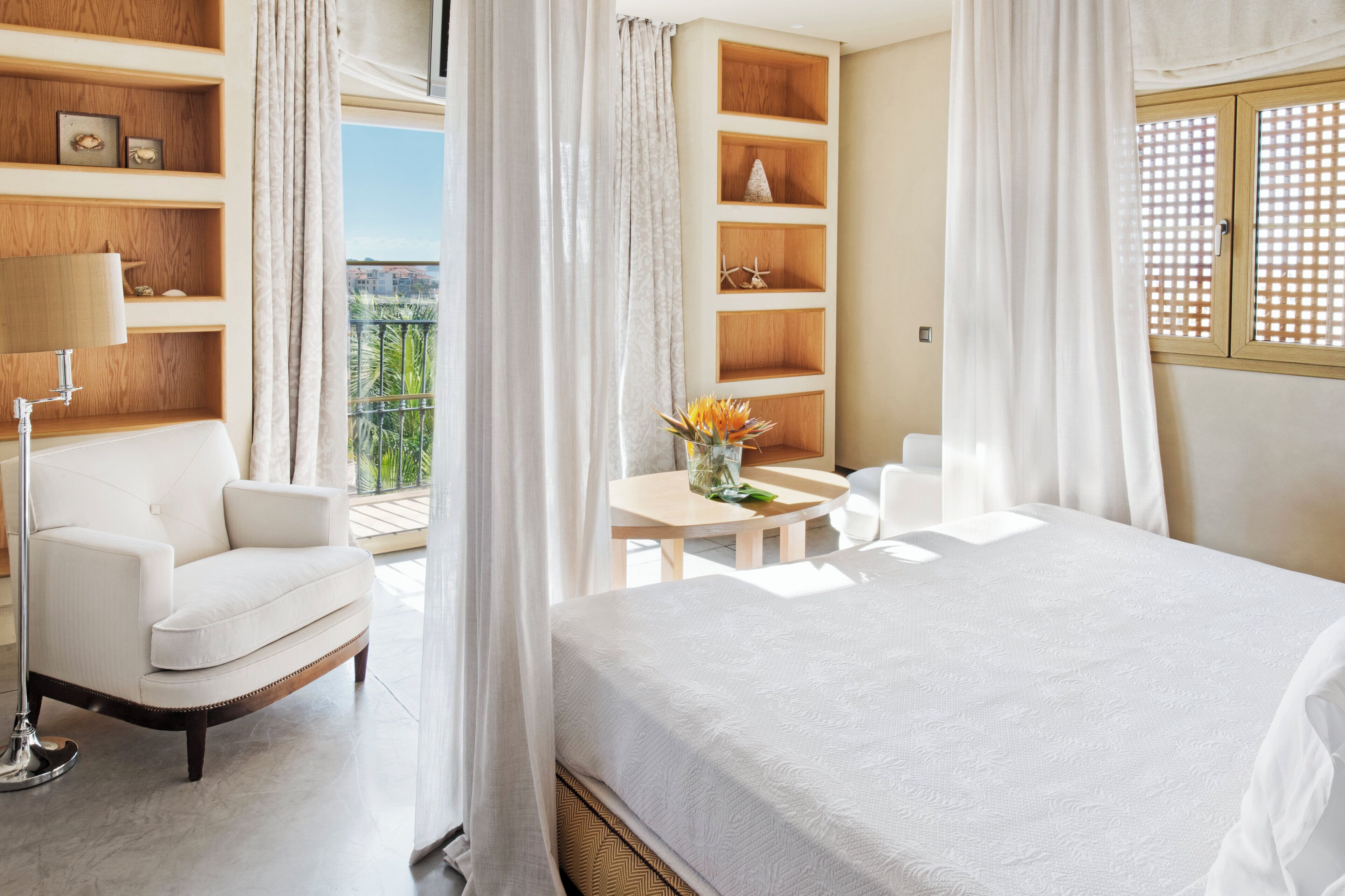 A hotel room with a bed, a chair, a table, and a balcony with a view.