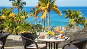 A dining table with plates, a vase with yellow flowers, and a glass pitcher of orange juice, overlooking a beach with palm trees and the ocean. - Bahia del Duque (Adeje)