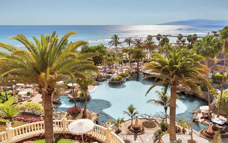 A resort with a large pool, palm trees, and a view of the ocean.