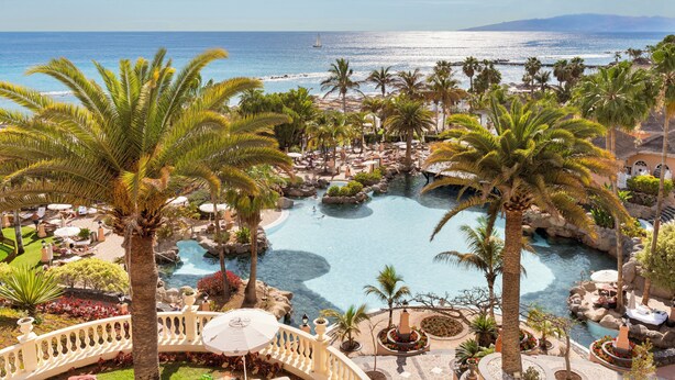 A resort with a large pool, palm trees, and a view of the ocean. - Bahia del Duque (Adeje)