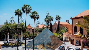 Una gran pirámide de cristal en una plaza rodeada de palmeras y coches estacionados.