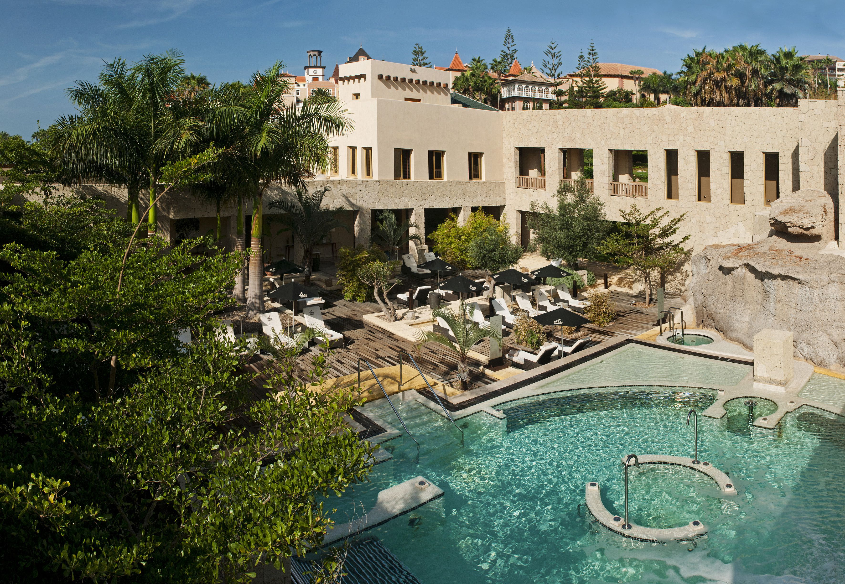 A resort with a swimming pool, lounge chairs, and palm trees.